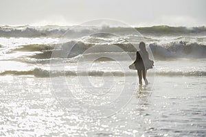 Back light shinny portrait of young happy Asian woman relaxed looking at wild sea waves on sunset tropical beach