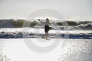 Silhouette of young happy Asian woman relaxed looking at wild sea waves on sunset tropical beach