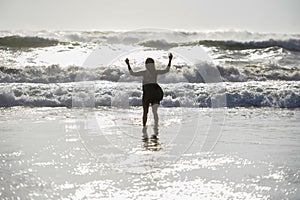 Silhouette of young happy Asian woman relaxed looking at wild sea waves on sunset tropical beach