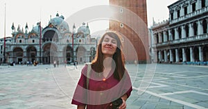 Back lit portrait of happy attractive brunette Caucasian tourist woman smiling at camera walking along San Marco Venice.