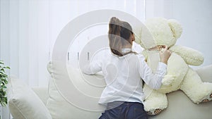 Back of little girl holding a tedy-bear, showing something behind the sofa.