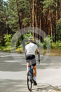 Back of a male cyclist rides outside the city on a bicycle in the woods on an asphalt road on a background of trees. Vertical