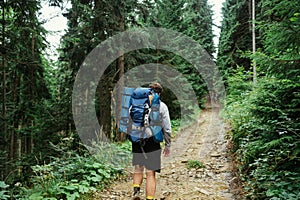 Back of a male tourist with a backpack on his back walks along a path in the mountains ahead