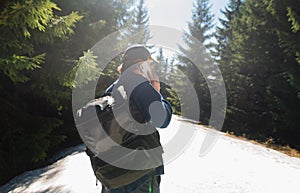 The back of a male tourist with a backpack on a walk in the snow in the spring in the mountains at the resort, talking on the