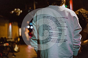 Back of a male wearing a sweatshirt with a poem written on it walking on the street