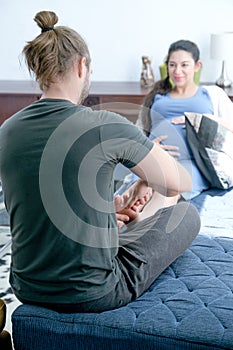 Back of man massage to foot and leg of his pregnant wife who sit on sofa in living room. Concept of good take care help to support