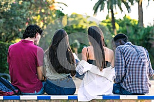 Back of a multracial group of students sitting on a bench outdoors studying