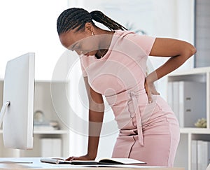 Back pain, bad posture and strain with a black woman in business suffering while working at her desk in the office