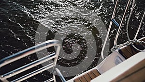 Back part of the sailboat, stern goes through the waves in lake. Sailing in the wind in sunny day. Close-up view.