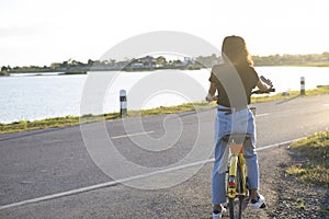 Back picture girl with yellow bicycle and river and road background at Sunset time
