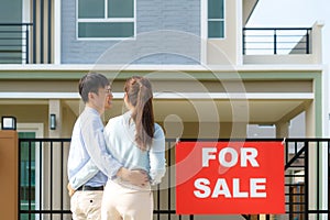 Back portrait of Asian young couple standing and hugging together looking happy in front of their new house to start new life.