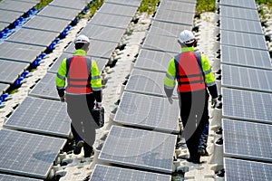 Back of professional with safety uniform walk on footpath along row of solar cell panels in workplace concept of green energy