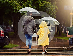 Back, raincoat or umbrella with a mother and daughter walking across a street in the city during winter. Autumn