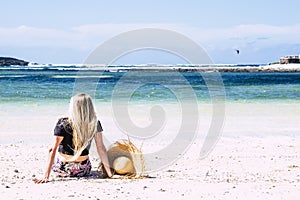 Back rear view of blonde long hair woman sit down on the sand at beach looking and enjoying blie ocean water and sky in summer