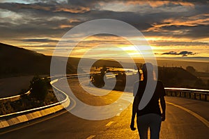 Back rear view of woman in hat walking on asphalt road at sunrise