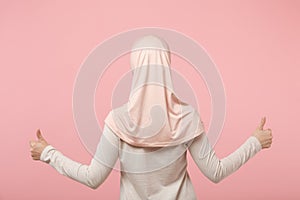 Back rear view of young arabian muslim woman in hijab light clothes posing isolated on pink background studio portrait