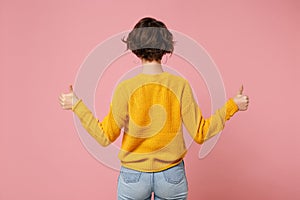 Back rear view of young brunette woman girl in yellow sweater posing isolated on pink wall background studio portrait