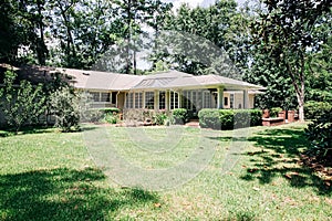 Back Rearview of exterior white cream brick 1950`s house with black shutters and a large lawn lot