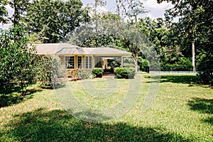 Back Rearview of exterior white cream brick 1950`s house with black shutters and a large lawn lot