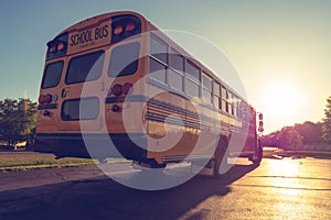 Back right low angle view of American Public school bus driving away with sunset in the distance