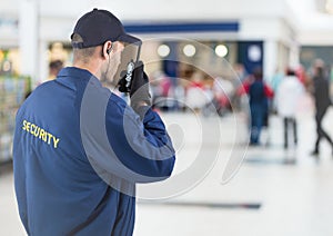 Back of security guard with walkie talkie against blurry shopping centre
