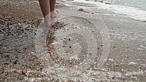 Back shooting of beautiful and sexy female legs walking forward along the sandy ocean. Slender female feet walk along