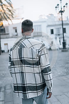 Back shot of a Caucasian young man with a checks shirt walking in the street