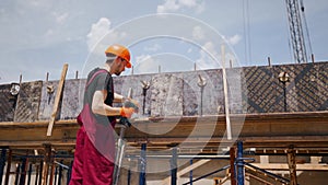 Back shot of professional construction worker in hard hat and bib overall makes formwork with electric screwdriver for