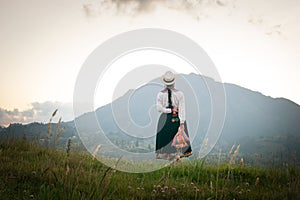 Back shot of Saraguro native girl walking wearing traditional regalia looking at a big mountain photo