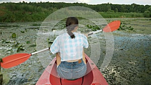 Back shot of young woman floating in red canoe on river. Female tourist is kayaking on lake on sunny day. Girl traveller is explor