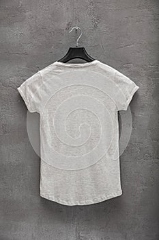 Back side of female grey melange cotton t-shirt on a hanger and a concrete wall in the background