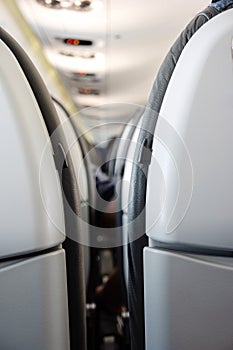 Back side of generic airplane seats next to each other shallow depth of field view forward to passengers