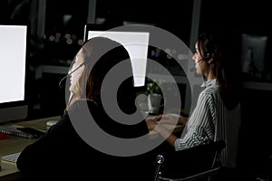 Back side of night shift staff group with headphone work at call center customer service desk at night, looking at desktop