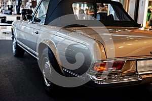 Back and side view of beige retro cabriolet car with close up of left chrome backlight, disc and mirror, wheel arch