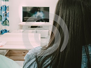 Back side view of black hair woman sit, relax and watch TV in he