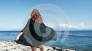 Back side view. Girl looks on ocean, black tunic, hair flutters in wind, slow motion