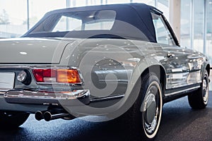 Back and side view of grey retro cabriolet car with close up of right chrome backlight and exhaust pipe, wheel arch