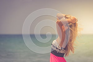 A back side view on a wonderful young woman watching to sea and raising her hands on sunrise