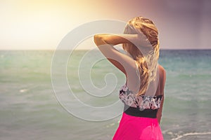 A back side view on a wonderful young woman watching to sea and raising her hands on sunrise