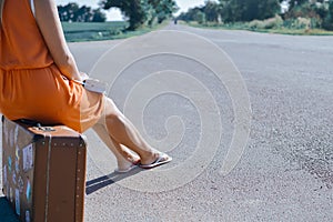 Back side view of young pretty woman hitchhiking waiting along the road for a ride