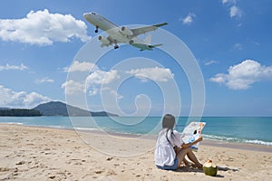 Back side of woman sitting on the beach and looked map, Background at the flying plane above the sea.