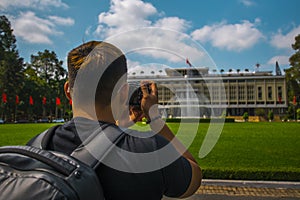 Back side of Young Asian traveling men taking a photo of Independence Palace in Ho Chi Minh City, Vietnam