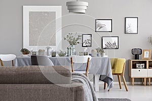 Back of a sofa and dining table with tableware, and graphics on a wall in a daily room interior
