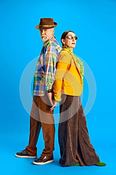 Back to back. Supportive, stylish couple, senior man and woman in fashionable clothes standing against blue studio
