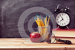 Back to school background with books and alarm clock over chalkboard