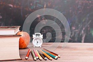 Back to school background with books, pencils, clock and apple on a wooden table