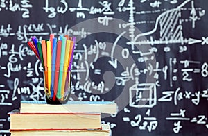 Back to school background with colorful felt pens and blurred math formulas written by white chalk on the black school