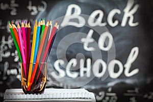 Back to school background with colorful pencils and the title Back to school written by white chalk on the black school