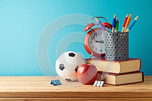Back to school background with pencils, football ball, books, apple and alarm clock on wooden table over blue background