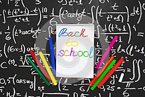Back to school background with title Back to school written on the white page of notebook on the chalkboard with math